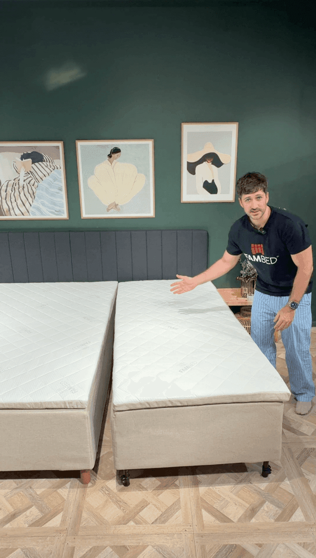 Ein Mann zeigt das Erweiterungsbett auf Rollen, das direkt an das vorhandene Bett herangerollt ist