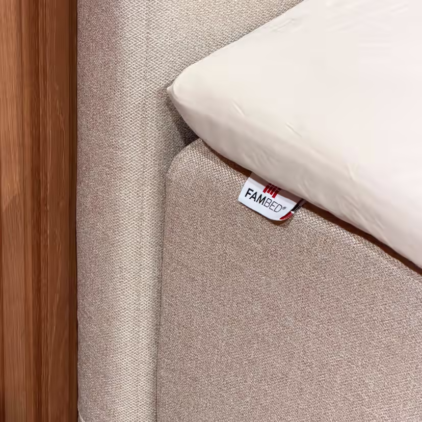 Nahaufnahme des beigen Bezugs um die Bettecke, mit FAMBED-Etikett und weißem Laken darüber